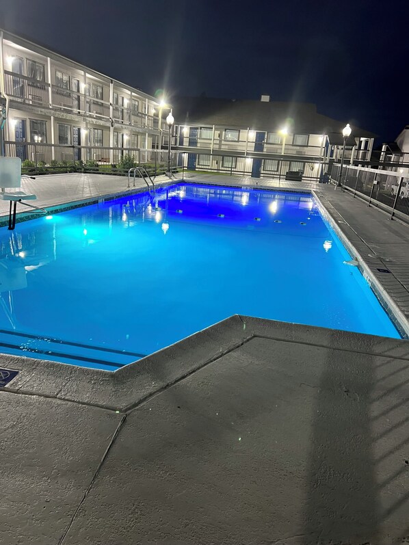 A swimming pool with a blue tint, surrounded by a building with balconies and railings.