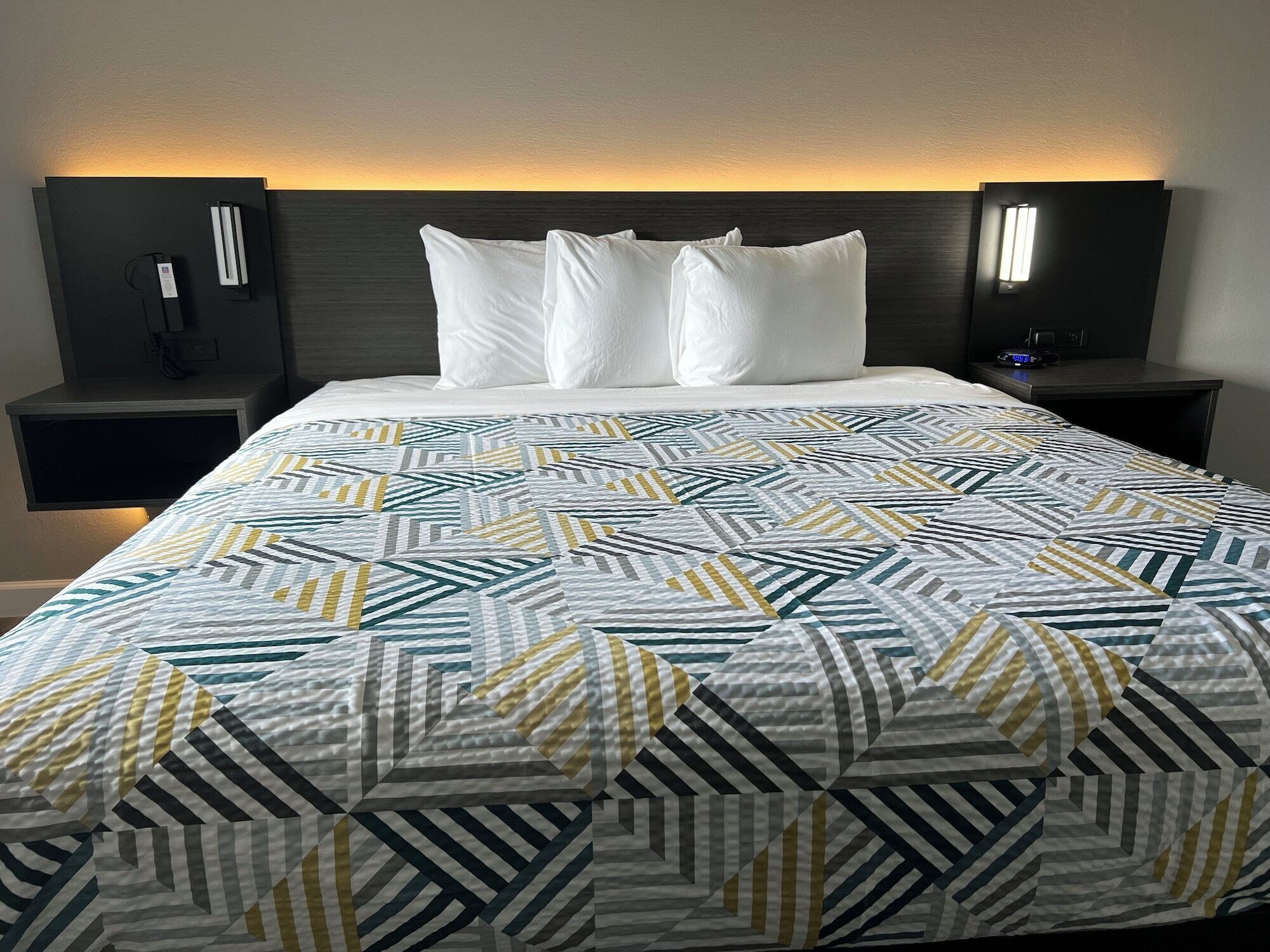 A neatly made bed with a geometric patterned bedspread, two bedside tables with lamps, and a dark headboard.