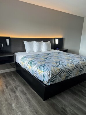A modern hotel room with a large bed, a bedside table, and a nightstand.