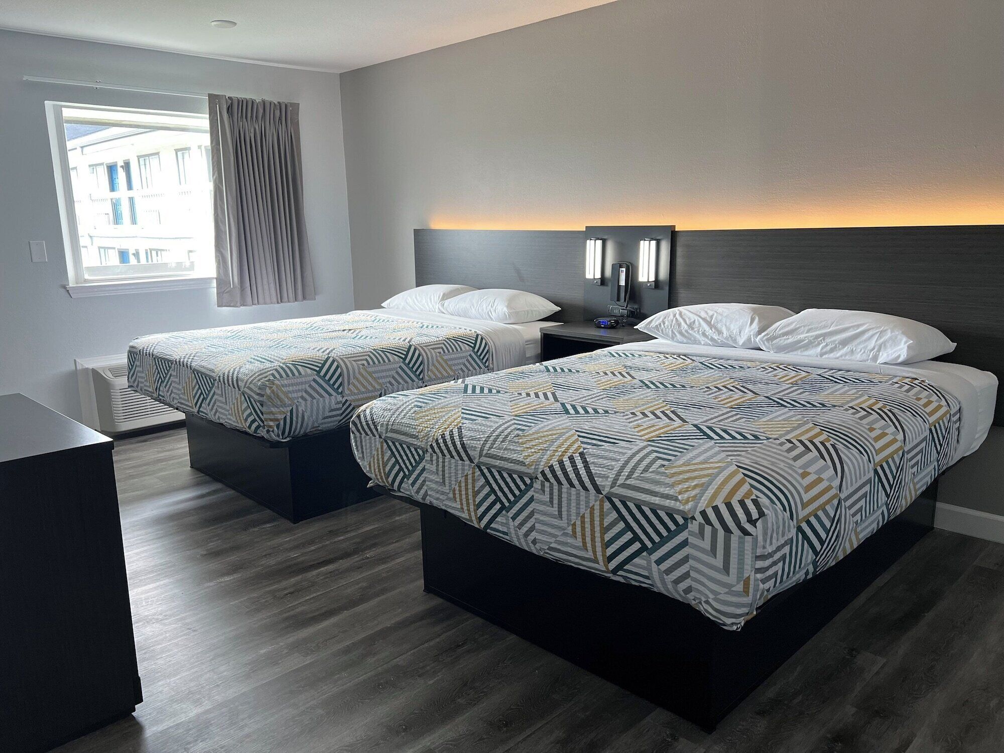 A hotel room with two beds, a nightstand, a desk, and a window with curtains.