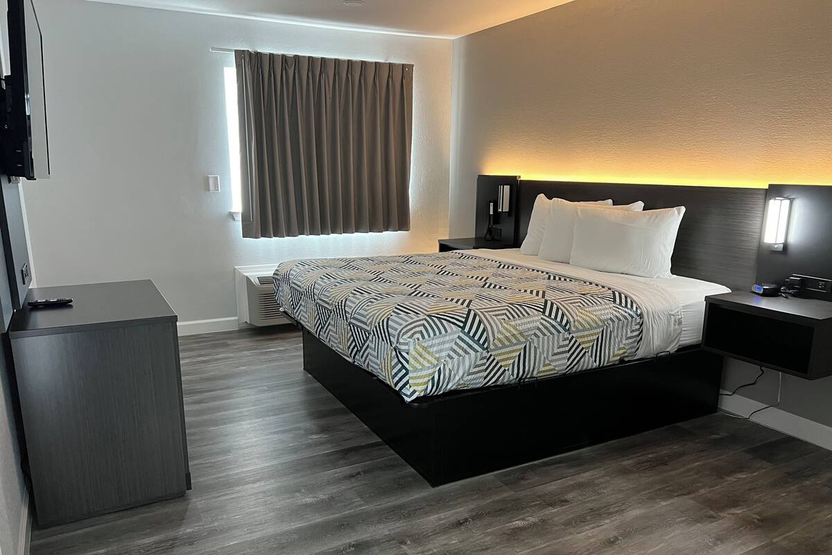 A modern hotel room with a large bed, bedside tables, a TV, and a window with curtains.