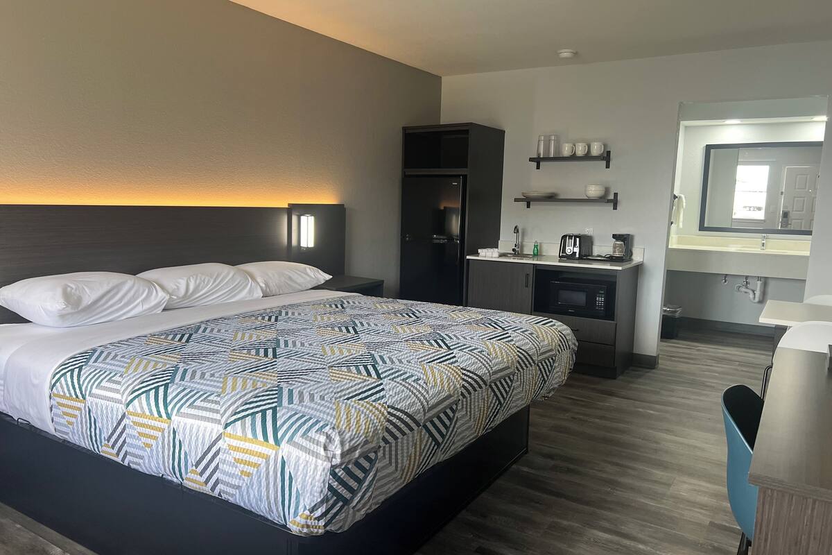 A hotel room with a bed, bedside table, microwave, and a small kitchenette.