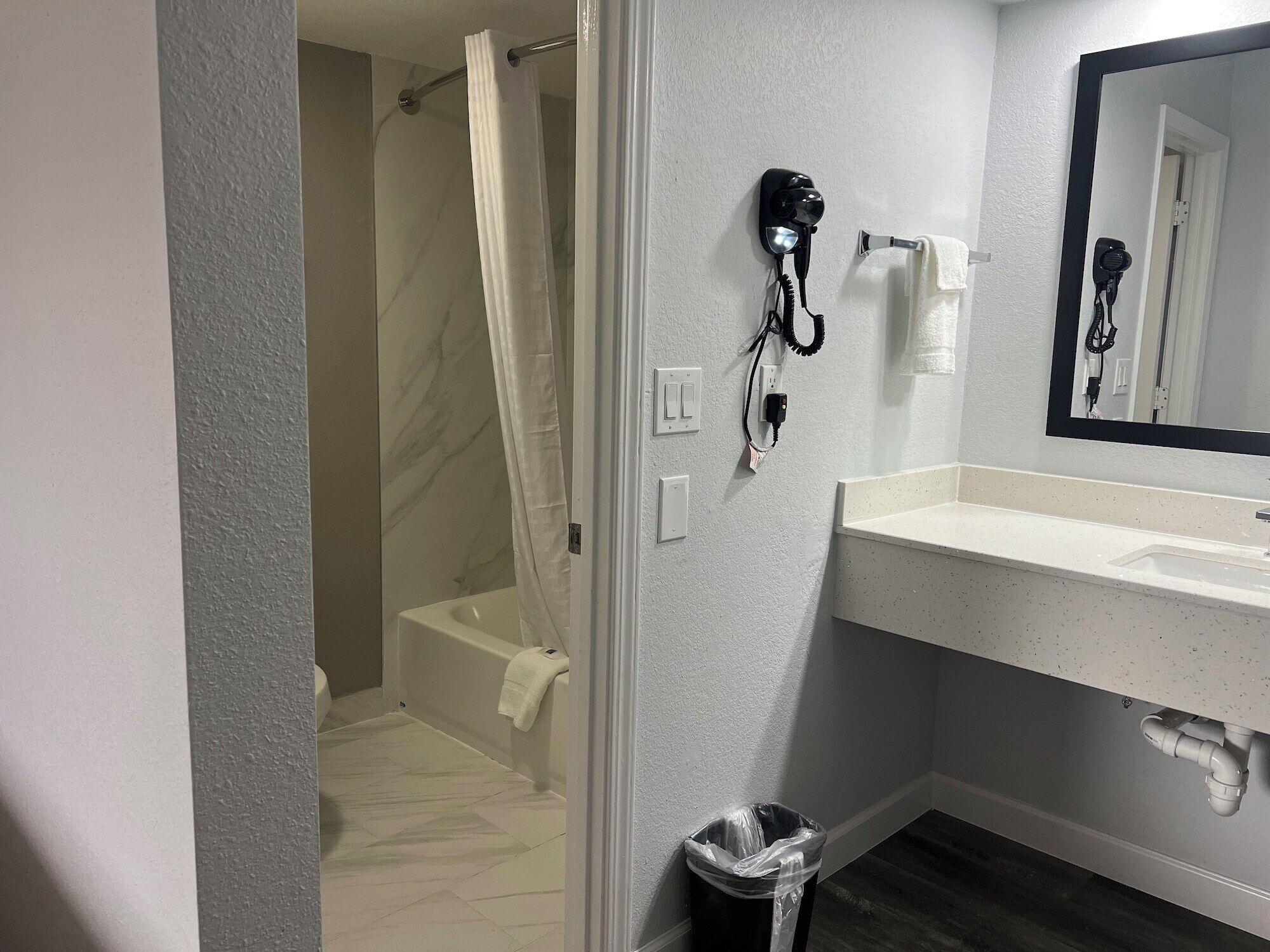 Ein Badezimmer mit Dusche, Waschbecken, Fön und Mülleimer.