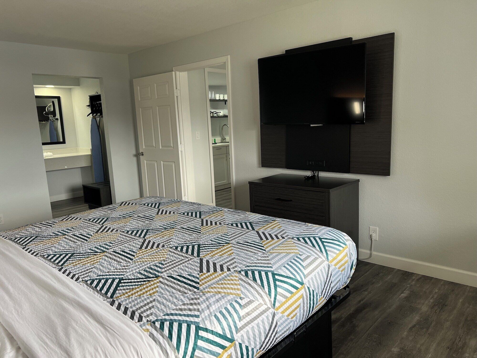 A bedroom with a bed, a dresser, a TV mounted on the wall, and a door leading to a bathroom.