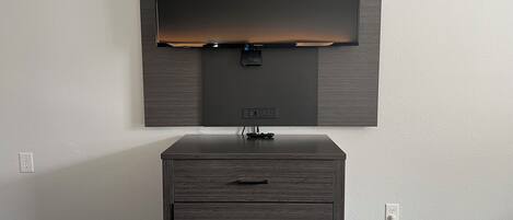 A modern room with a flat-screen TV mounted on the wall, a wooden dresser with drawers, and two beds with striped bedding.