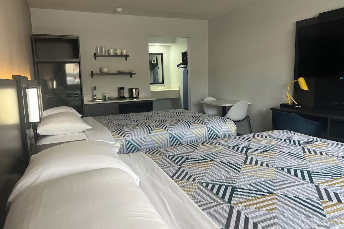 A hotel room with two beds, a desk, a chair, a TV, and a bathroom visible through an open door.