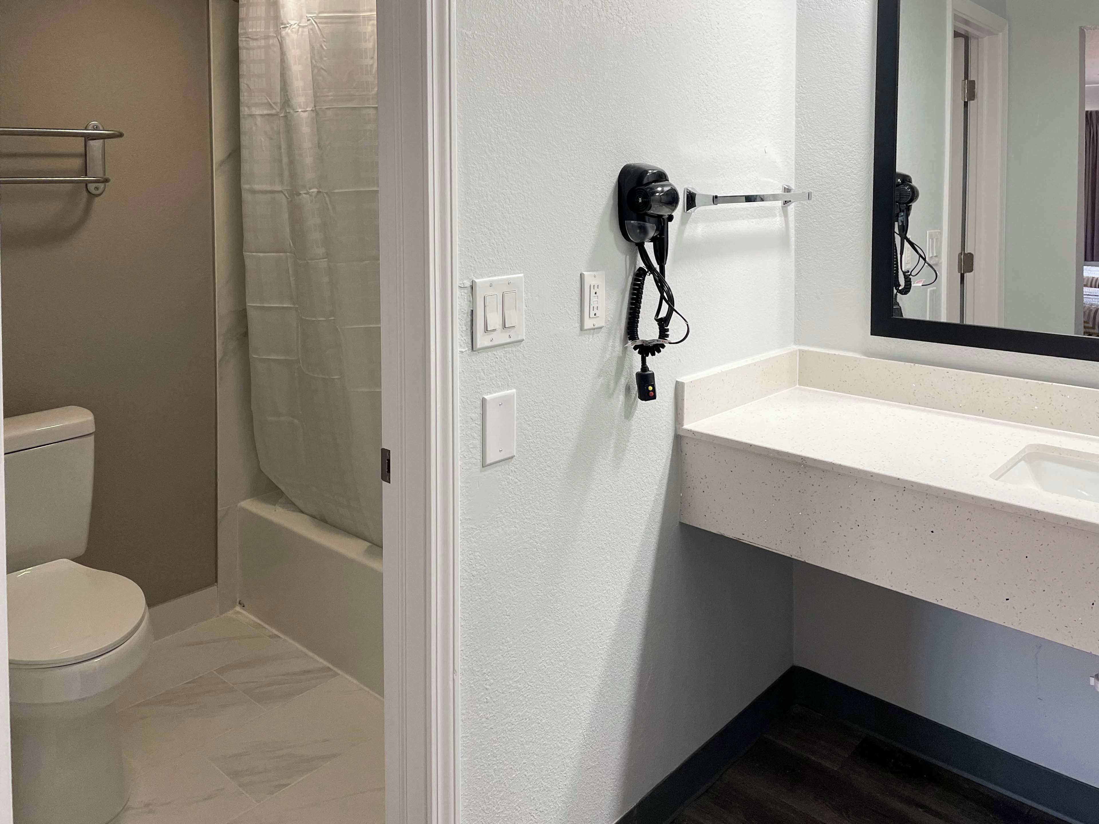 A bathroom with a white toilet, a shower with a glass door, a white sink, and a hairdryer mounted on the wall.