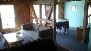 A cozy room with a sofa, a small table, and a dining area with a table and chairs. - Attwood Creek Ranch (Lone Butte)