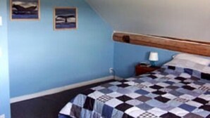 A bedroom with a checkered bedspread, wooden headboard, and two framed pictures on the wall. - Attwood Creek Ranch (Lone Butte)