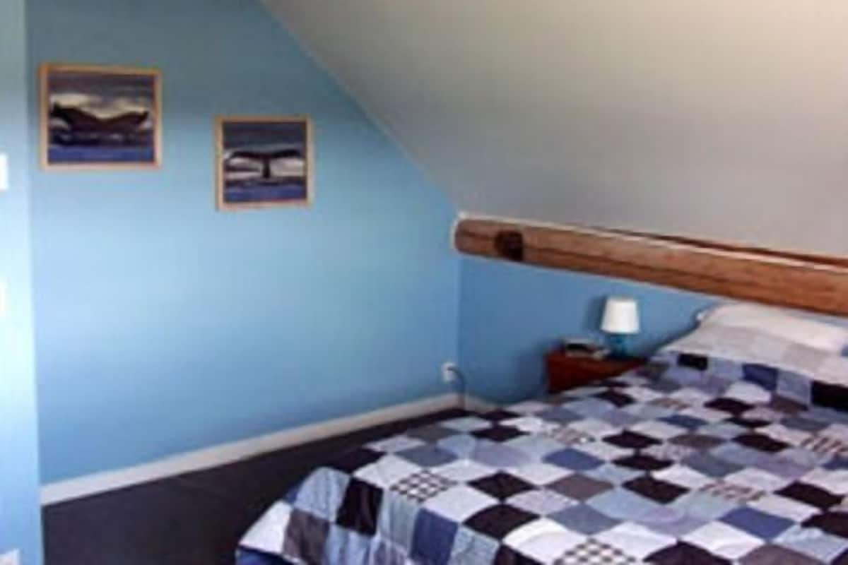 Une chambre avec une couvre-lit à carreaux, une tête de lit en bois et deux tableaux encadrés accrochés au mur.
