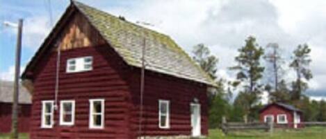 A red wooden house with a gabled roof, a front door, and two windows.