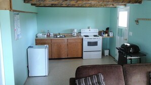 A compact kitchen with a refrigerator, stove, and coffee maker. - Attwood Creek Ranch (Lone Butte)