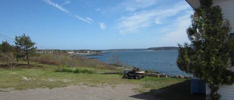 A gravel driveway leading to a building with a blue roof, overlooking a body of water and a distant shoreline.
