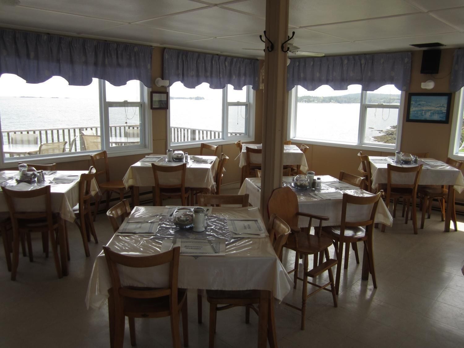 A restaurant with tables set for dining, large windows with views of the water, and a wooden interior.
