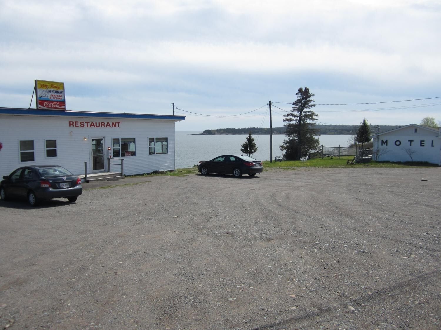 Un restaurante y motel con estacionamiento de grava y vistas al lago.