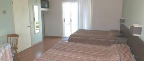 Een kamer met twee bedden, een stoel, een televisie en een raam met gordijnen.