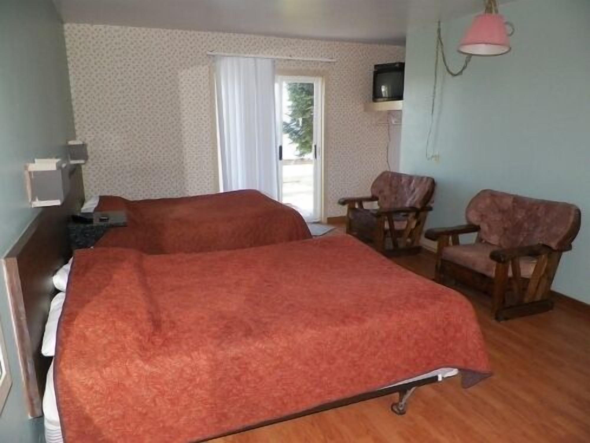 A room with two beds, a chair, a desk, and a television.