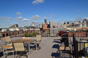 Une terrasse sur le toit, avec une table et des chaises, un barbecue et une vue sur le panorama de la ville.
