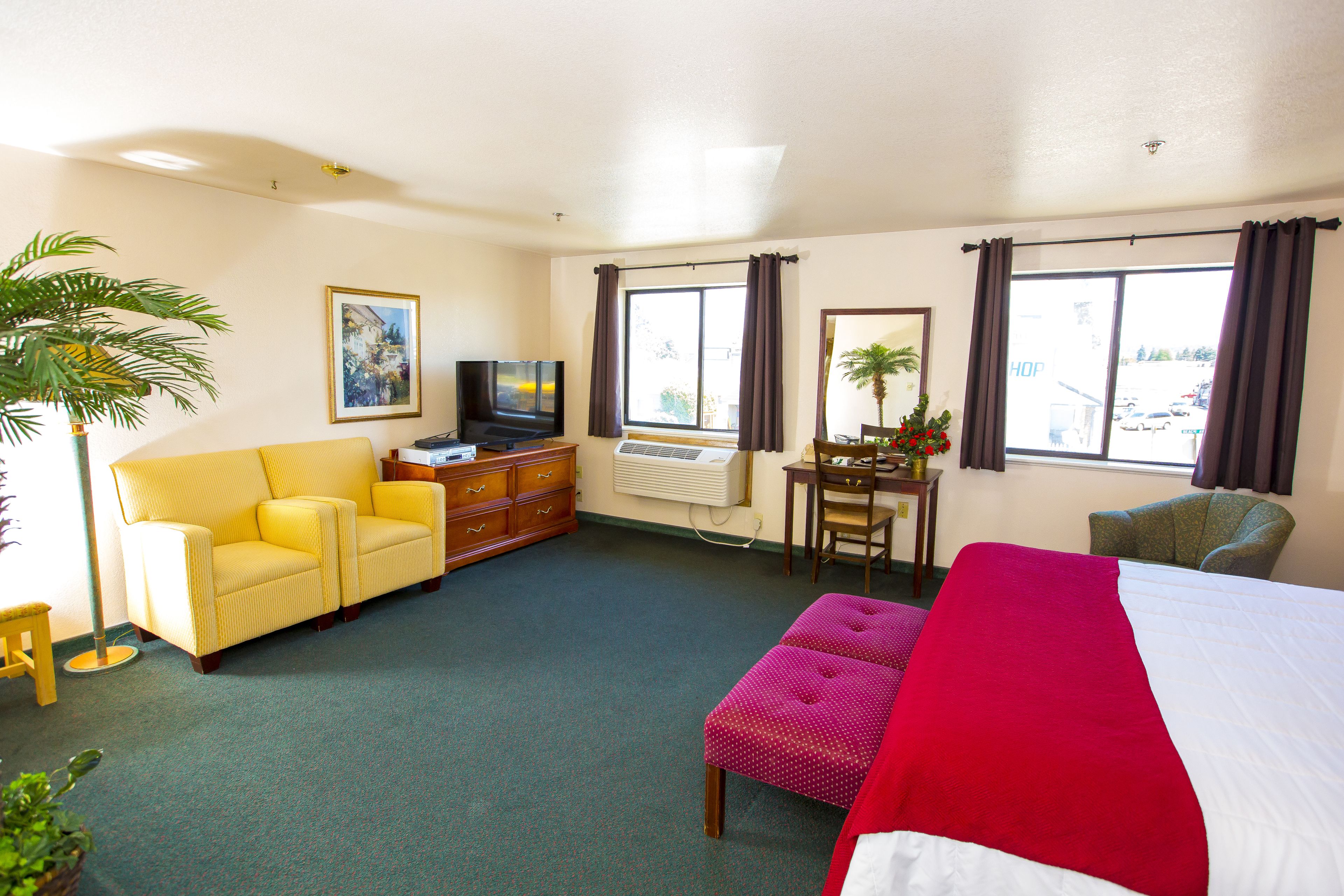 Una habitación de hotel con cama, sofá amarillo, televisión, escritorio y ventana con cortinas.