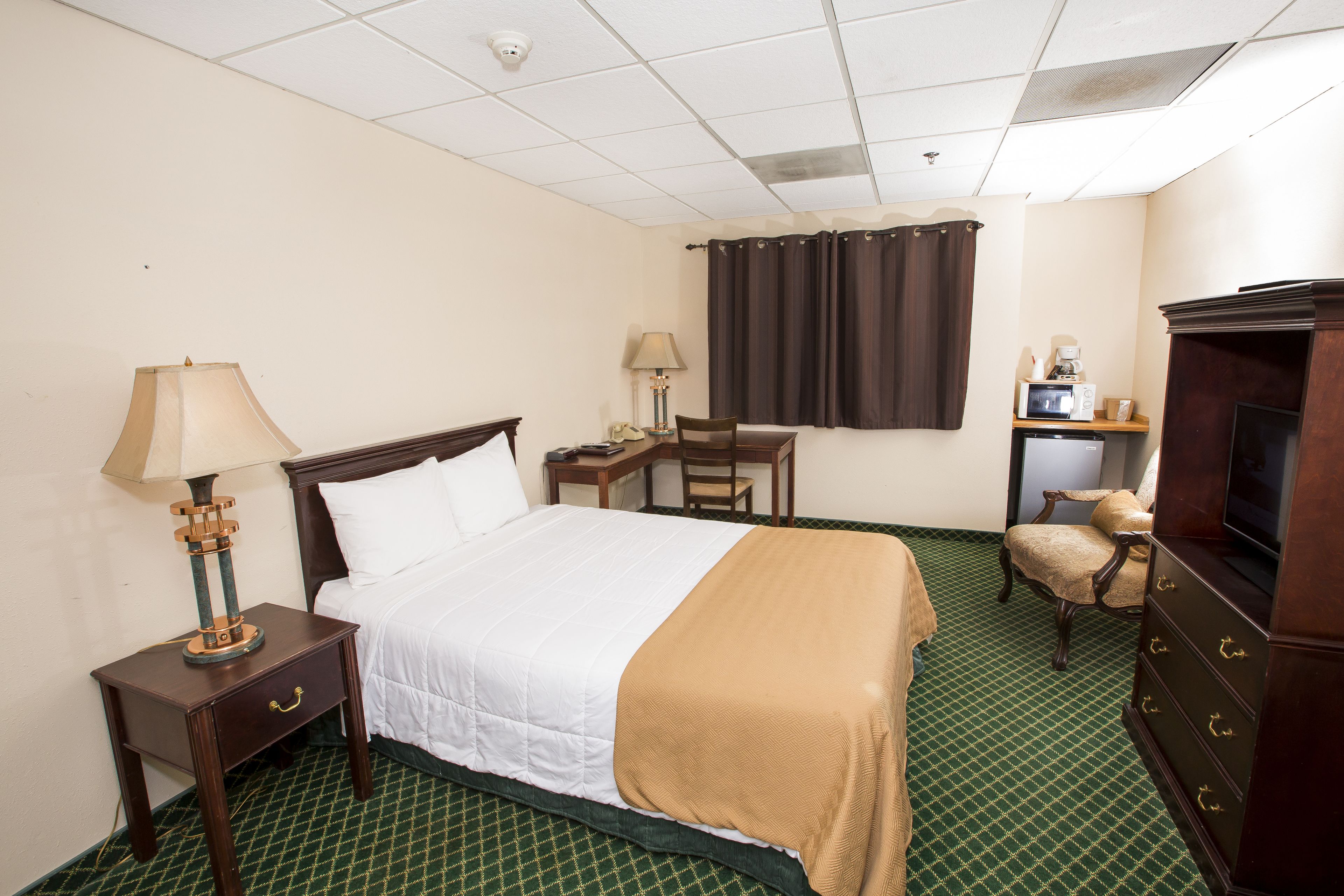 A hotel room with a bed, a desk, a chair, a television, and a dresser.