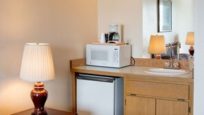 A hotel bathroom with a wooden vanity, a white sink, a microwave, a coffee maker, and a lamp. - Village Inn & Suites (Marysville)
