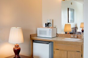 A hotel bathroom with a wooden vanity, a white sink, a microwave, a coffee maker, and a lamp. - Village Inn & Suites (Marysville)