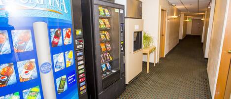A hallway with vending machines, a plant, and a door at the end.