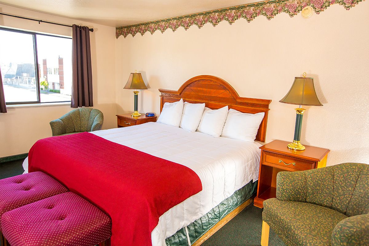 A hotel room with a large bed, two bedside tables, a chair, and a window with curtains.