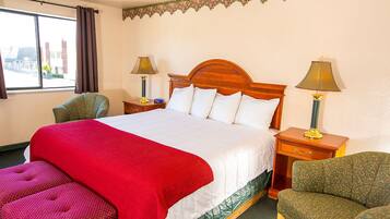 A hotel room with a large bed, two bedside tables, a chair, and a window with curtains.