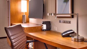 Habitación de hotel con escritorio de madera, televisor de pantalla plana, cafetera, teléfono y lámpara.