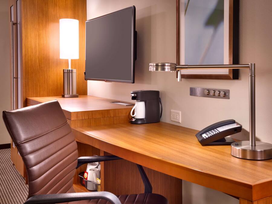 Habitación de hotel con escritorio de madera, televisor de pantalla plana, cafetera, teléfono y lámpara.