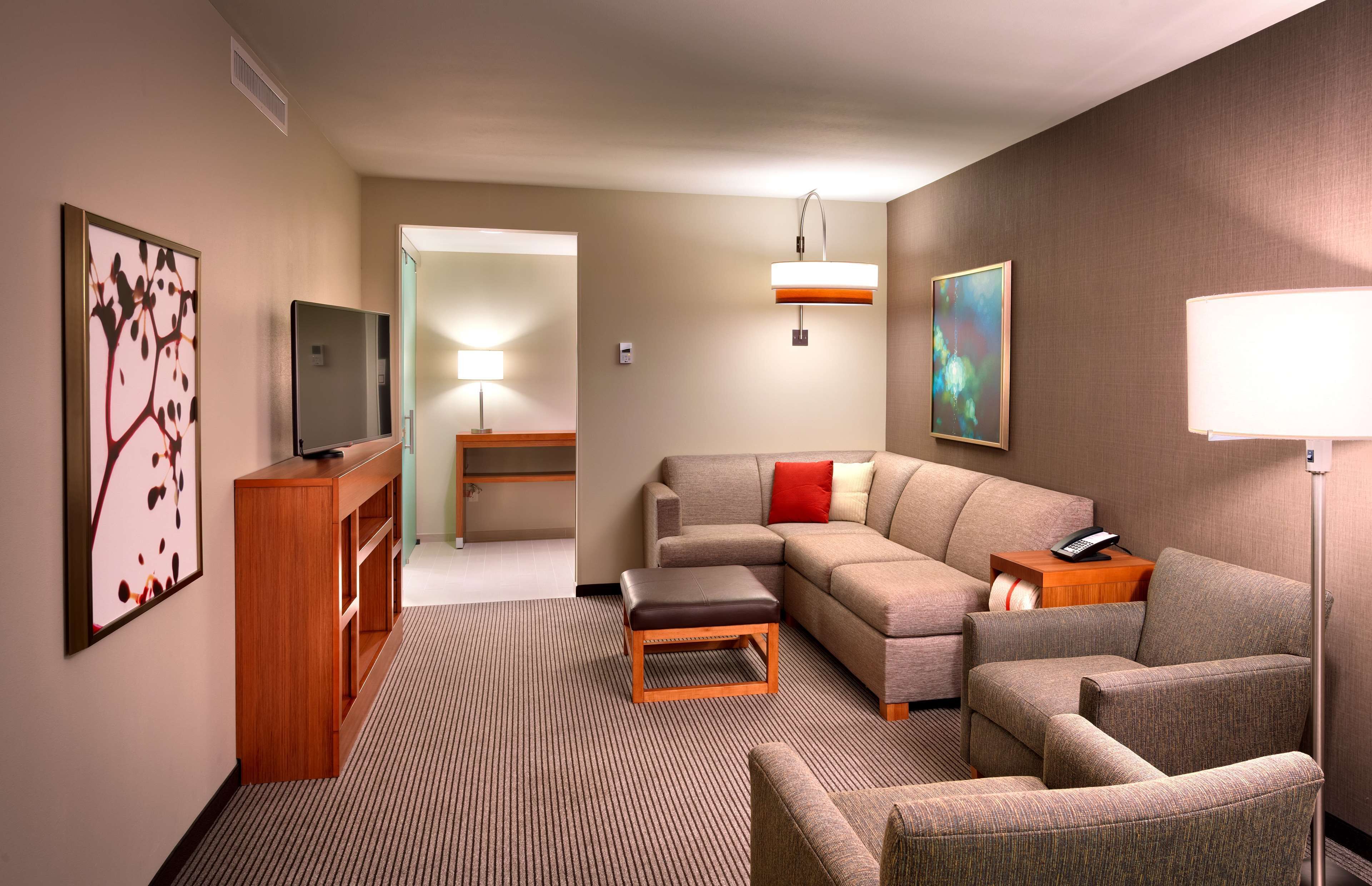 A modern hotel room with a sofa, armchairs, a small table, a TV, and a lamp.