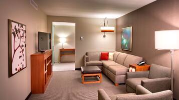 A modern hotel room with a sofa, armchairs, a small table, a TV, and a lamp.