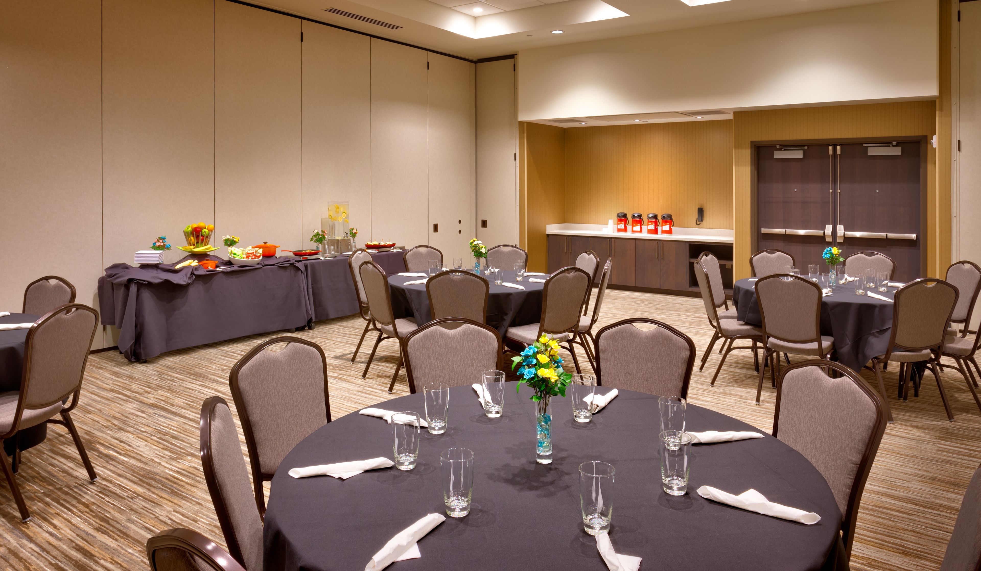 A conference room with round tables, chairs, and a buffet area.