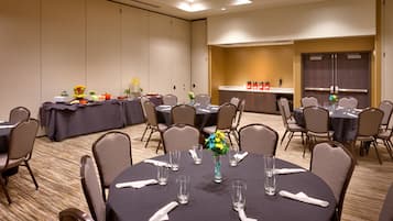 Une salle de conférence équipée de tables rondes, de chaises et d’un espace buffet.