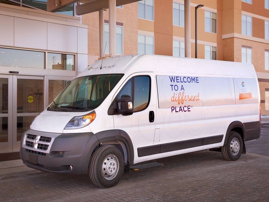 A white van parked in front of a building with a sign that reads "Welcome to a different place."