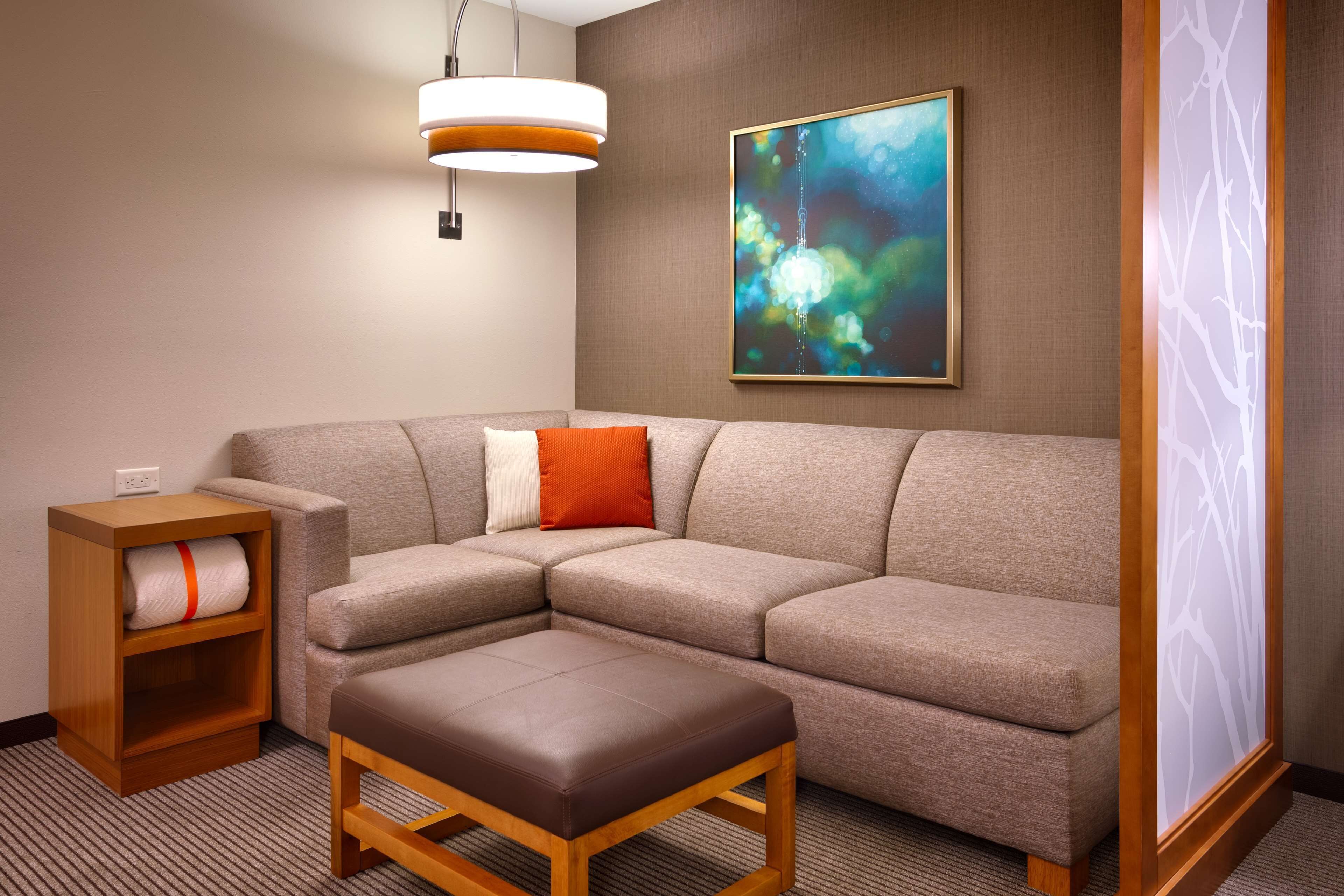 A modern living room with a sectional sofa, a wooden side table, a bench, a wall-mounted light fixture, and a framed abstract painting.