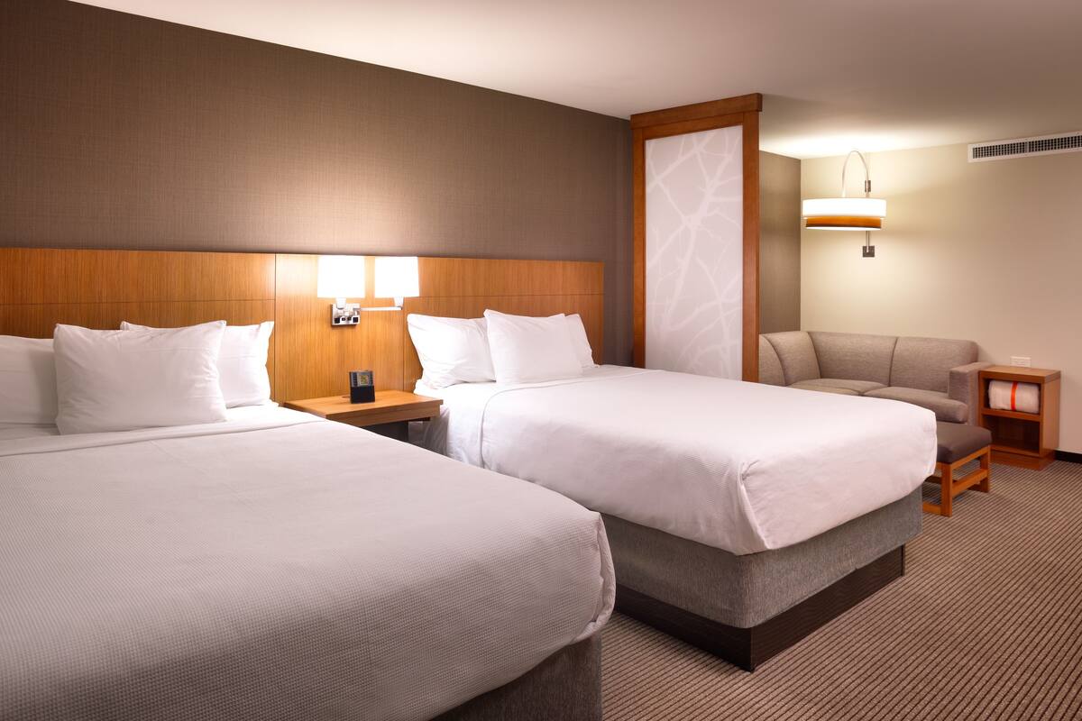 A hotel room with two beds, a sofa, a nightstand, and a lamp.