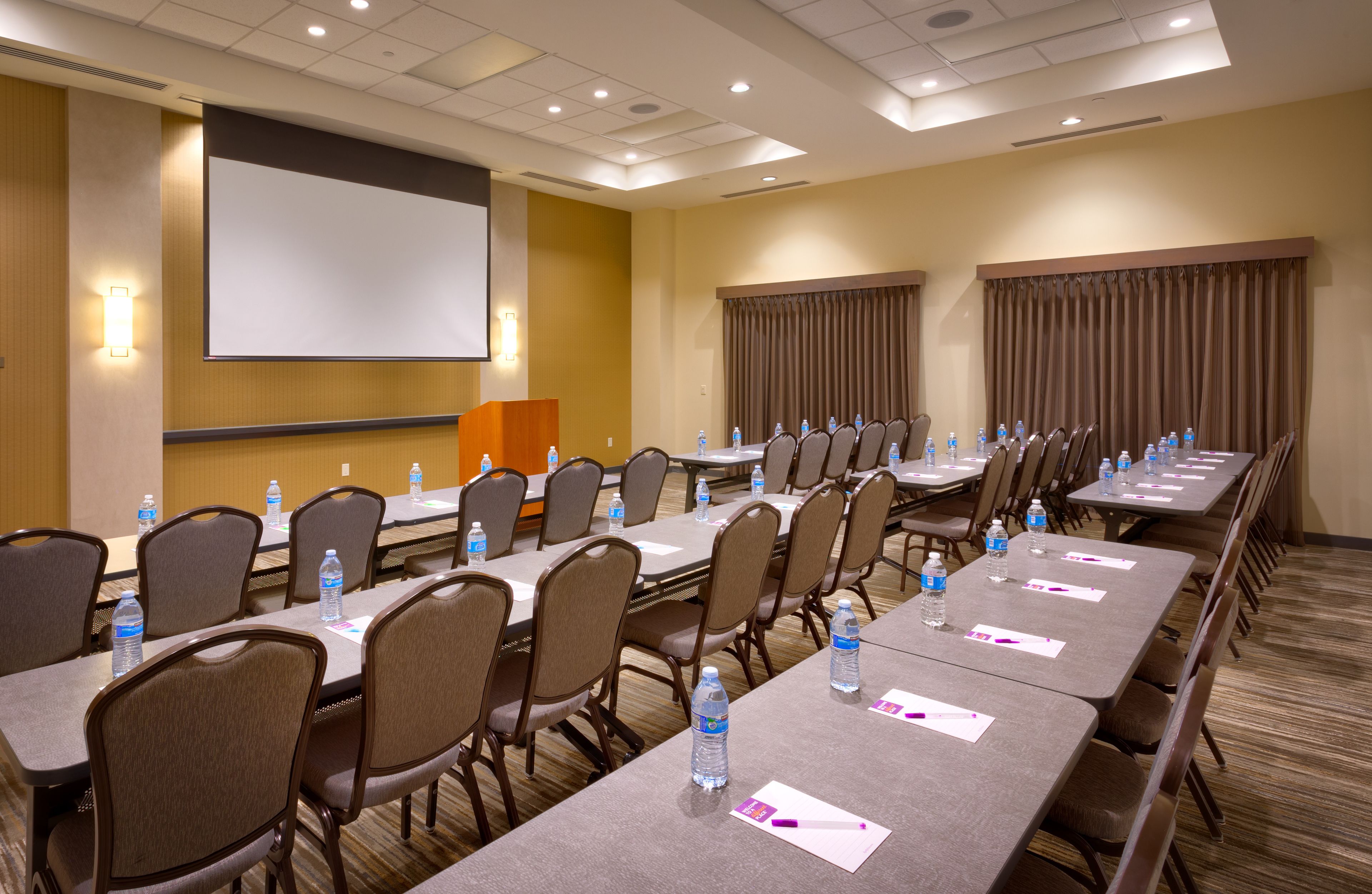 A conference room with multiple tables, chairs, and a large screen.