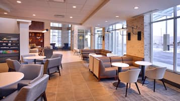 A modern cafe with seating arrangements, a coffee bar, and large windows offering a view.