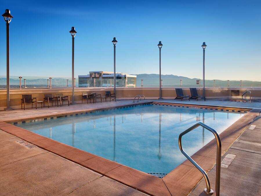 A rooftop pool with clear blue water, surrounded by lounge chairs and a modern building in the background.