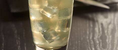 A glass of a clear beverage with ice cubes and a lime slice, on a dark wooden table.