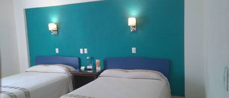 A hotel room with two single beds, teal-colored walls, and wall-mounted lights.