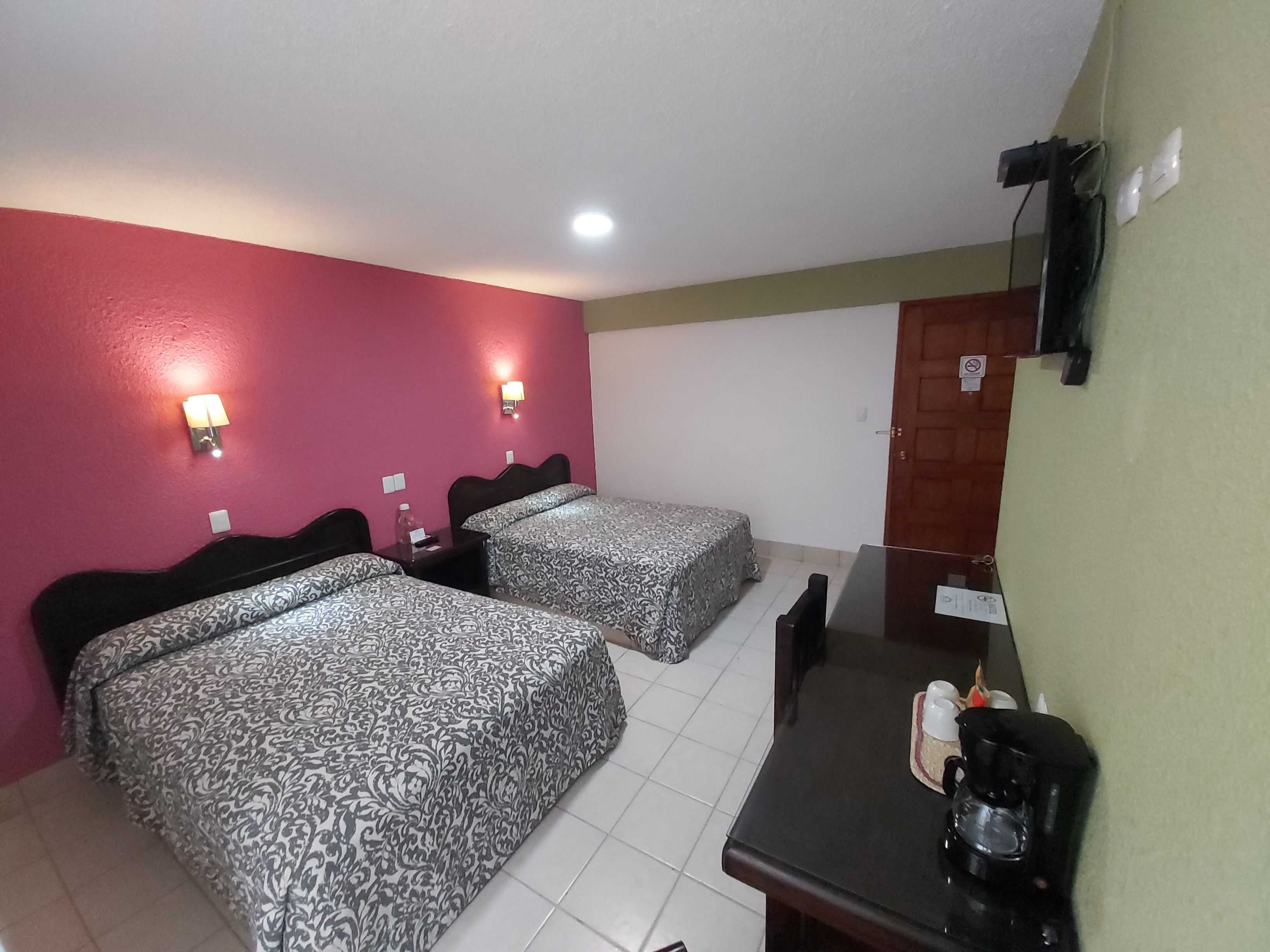 A hotel room with two beds, a desk with a coffee maker, and a TV mounted on the wall.
