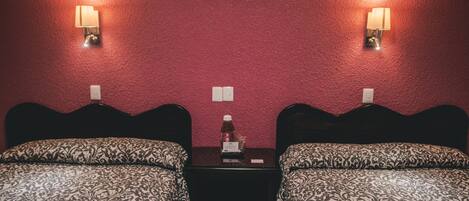 Habitación de hotel con dos camas, cada una con una colcha estampada, una mesita en el centro y lámparas fijadas a la pared.