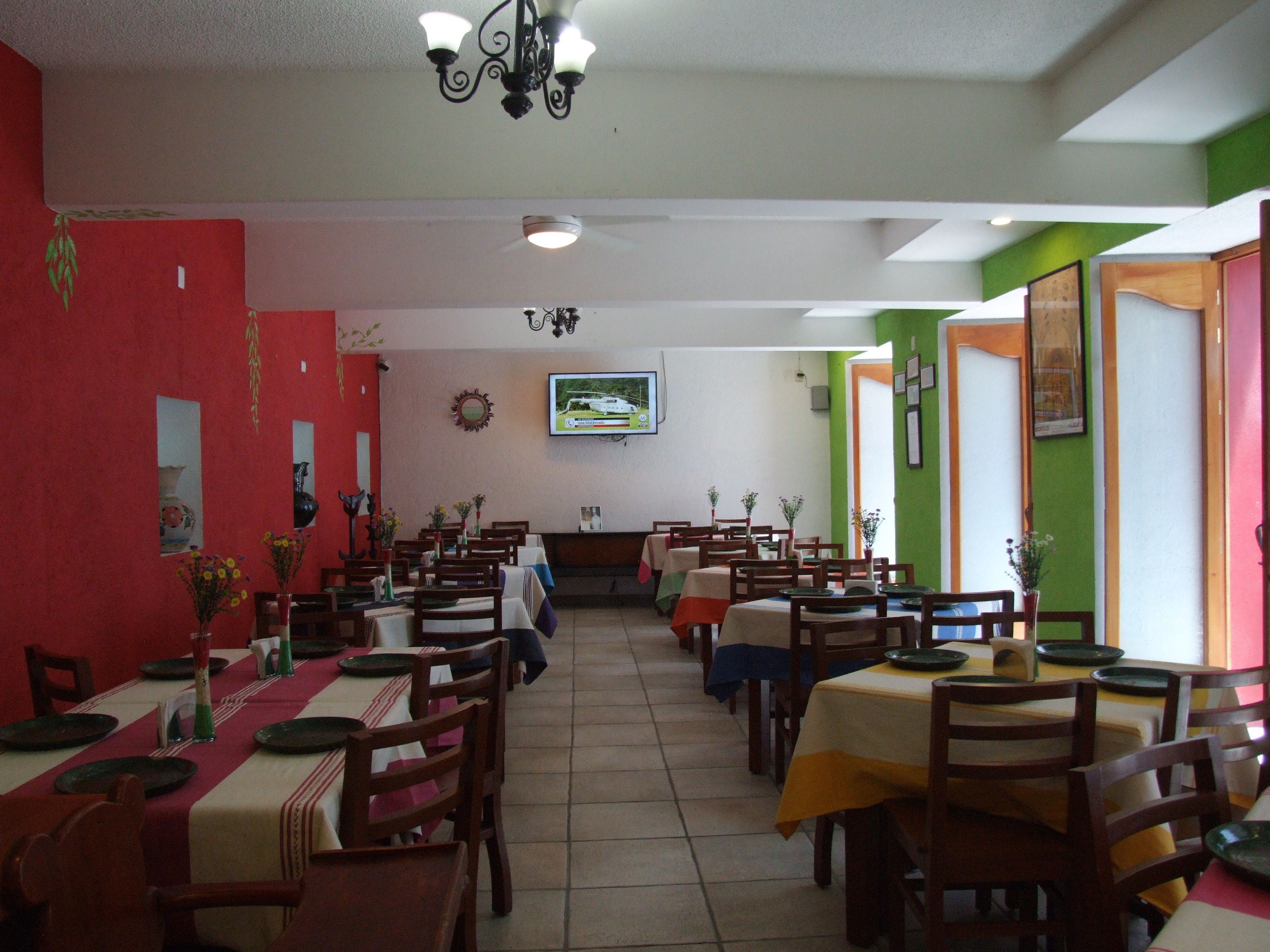 A restaurant with multiple tables and chairs, a television mounted on the wall, and a ceiling fan.