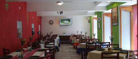 Un restaurante con varias mesas y sillas, un televisor montado en la pared y un ventilador de techo.