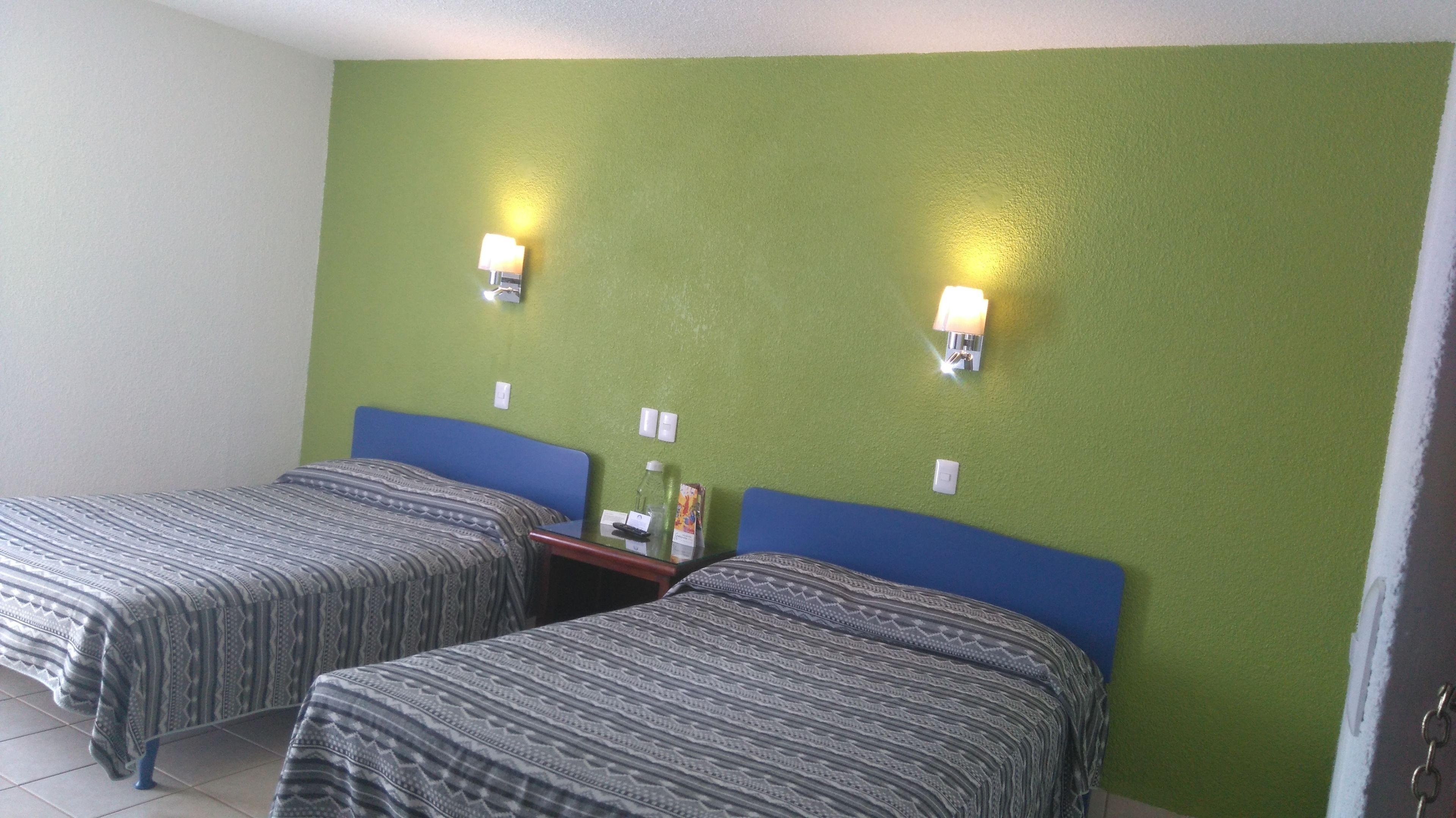 Una habitación con dos camas, paredes verdes y dos luces fijadas a la pared.