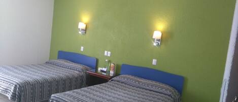Una habitación con dos camas, paredes verdes y dos luces fijadas a la pared.