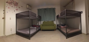 Une chambre avec des lits superposés, un fauteuil vert et une fenêtre avec des rideaux.